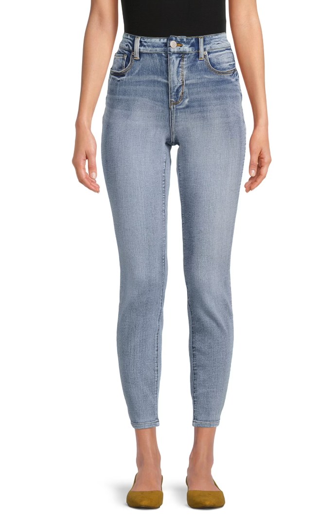 Woman wearing high-rise light wash skinny ankle jeans with gold flat shoes, front view on white background
