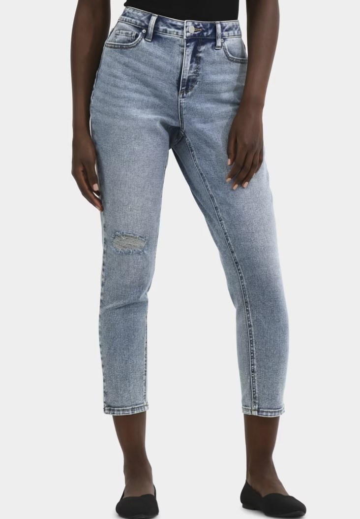Woman wearing high-rise light wash distressed slim mom jeans with ripped knee detail, front view on grey background